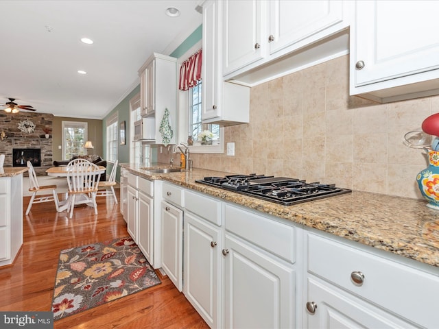 kitchen featuring black gas cooktop, light wood-style flooring, a large fireplace, a sink, and white cabinetry