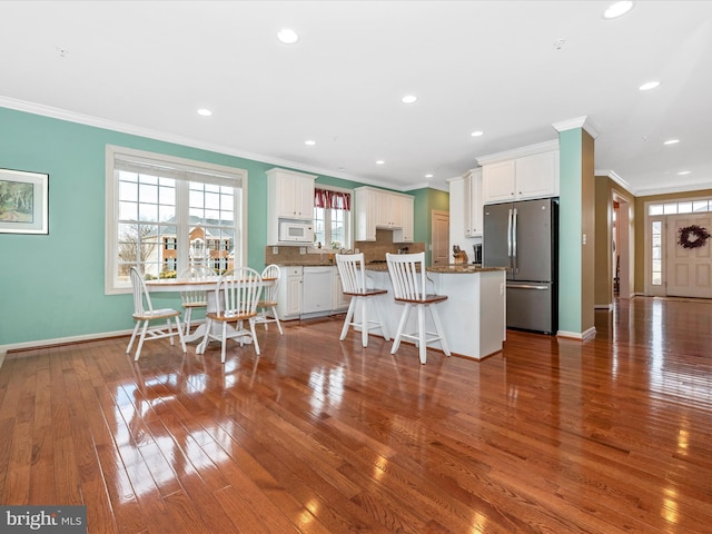 kitchen with white microwave, a kitchen island, white cabinetry, a kitchen breakfast bar, and freestanding refrigerator