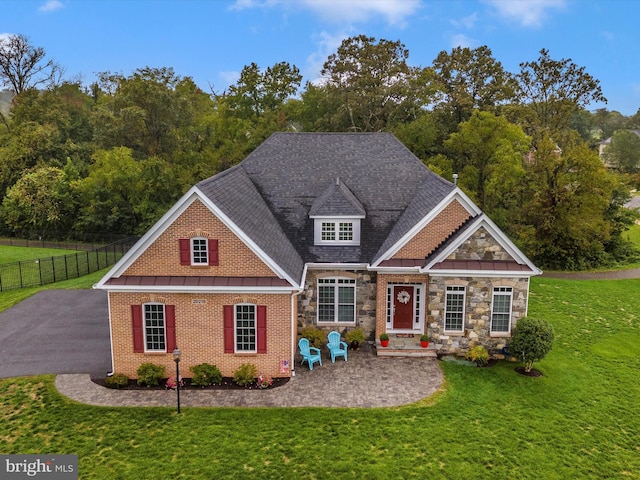 view of front facade with a patio, fence, stone siding, roof with shingles, and a front lawn