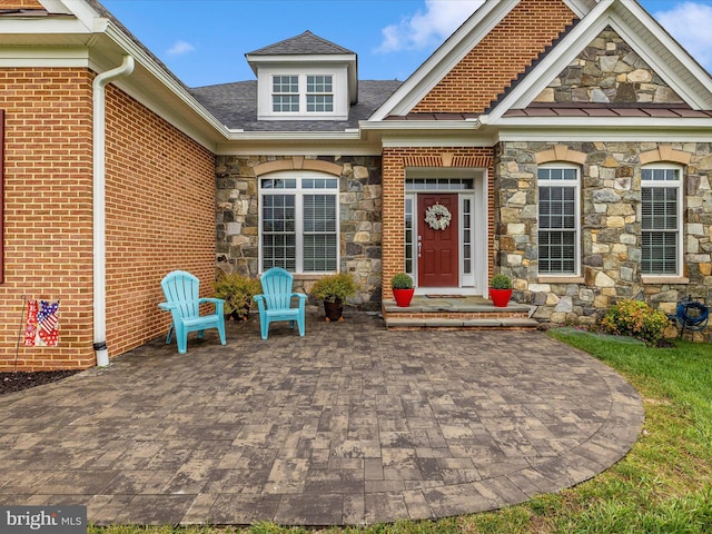 view of exterior entry featuring brick siding, stone siding, and a patio