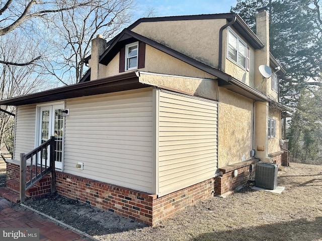 view of side of home featuring central air condition unit, stucco siding, a chimney, and entry steps