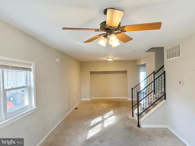 empty room with visible vents, stairway, a ceiling fan, light carpet, and baseboards