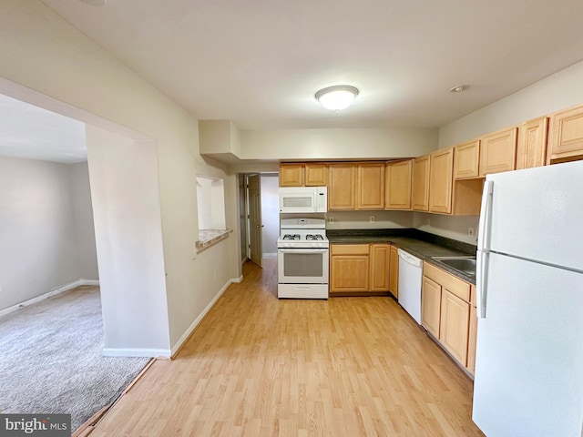 kitchen with dark countertops, a sink, light wood-type flooring, white appliances, and baseboards