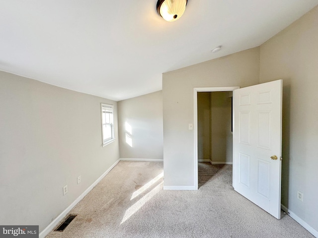 spare room featuring light carpet, baseboards, visible vents, and vaulted ceiling