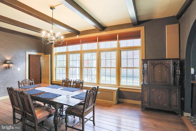 dining space featuring a notable chandelier, a textured wall, beamed ceiling, baseboards, and hardwood / wood-style flooring