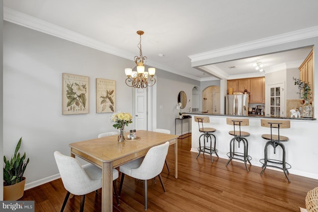 dining room featuring arched walkways, a notable chandelier, ornamental molding, wood finished floors, and baseboards