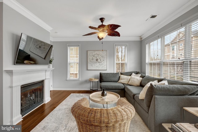 living area featuring baseboards, a glass covered fireplace, wood finished floors, and crown molding