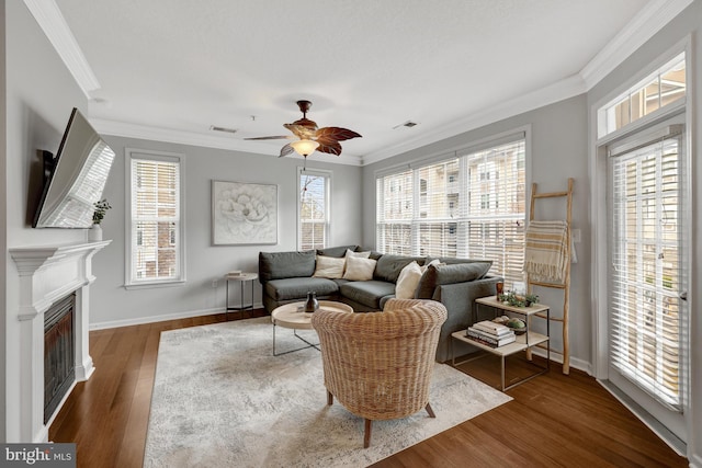 living area with baseboards, visible vents, wood finished floors, crown molding, and a fireplace