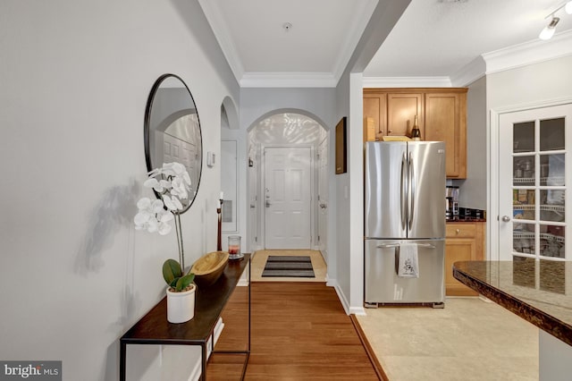 kitchen featuring brown cabinetry, dark countertops, freestanding refrigerator, crown molding, and light wood-style floors