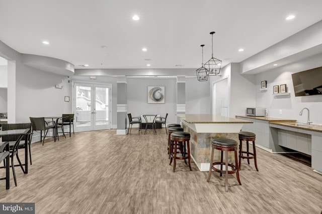 kitchen featuring light wood finished floors, modern cabinets, stainless steel microwave, a center island, and french doors