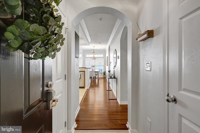 hall with ornamental molding, arched walkways, baseboards, and wood finished floors