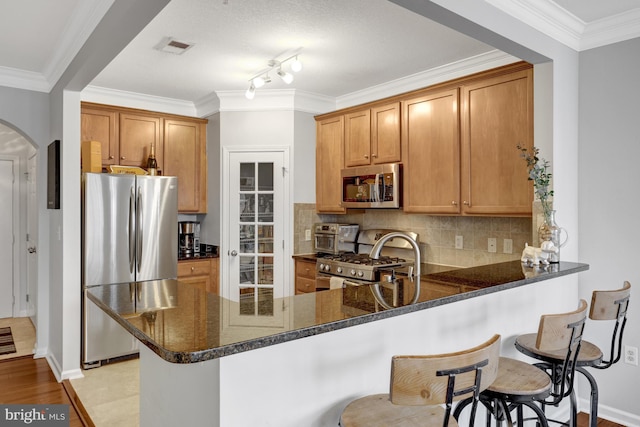 kitchen with visible vents, arched walkways, decorative backsplash, a peninsula, and stainless steel appliances