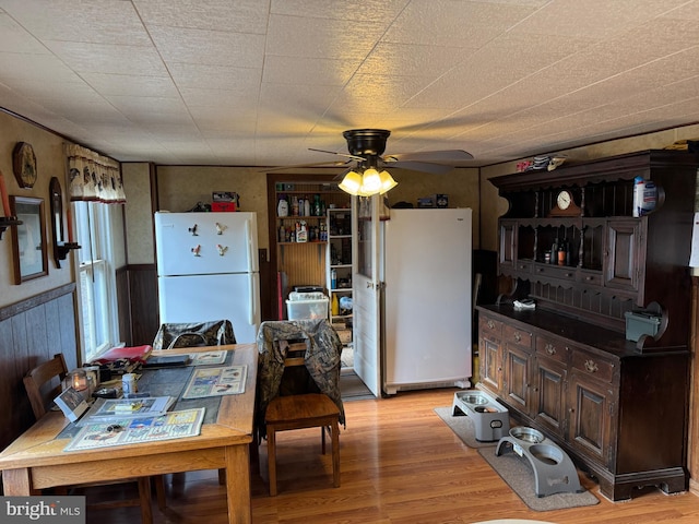 kitchen with freestanding refrigerator, a wainscoted wall, ceiling fan, and light wood finished floors