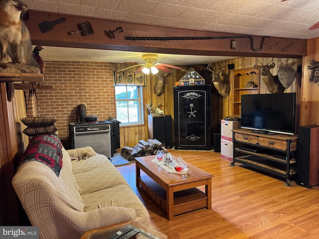 living area with a ceiling fan, wood walls, brick wall, and wood finished floors