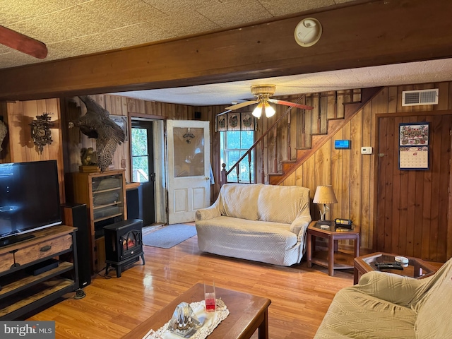 living room with visible vents, stairway, a wood stove, wooden walls, and wood finished floors