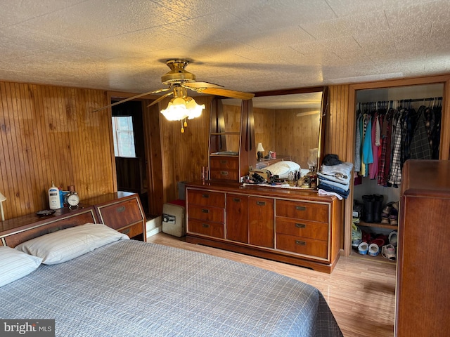 bedroom with light wood finished floors, a closet, a textured ceiling, and wood walls