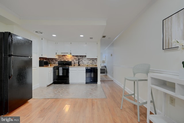 kitchen with light wood finished floors, light countertops, decorative backsplash, white cabinets, and black appliances