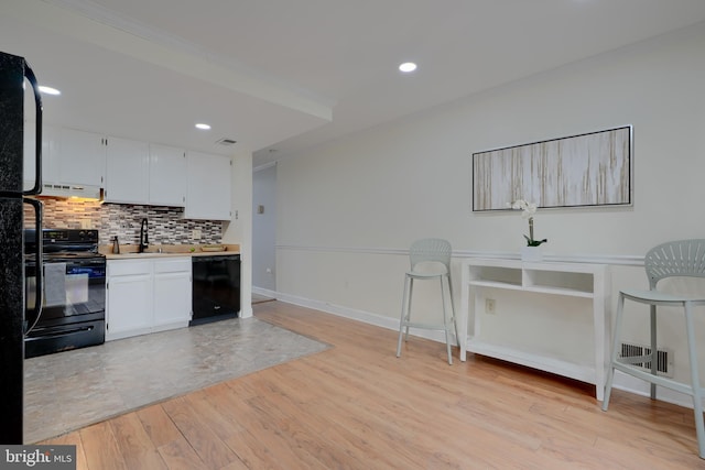 kitchen with white cabinets, light wood finished floors, range hood, black appliances, and tasteful backsplash