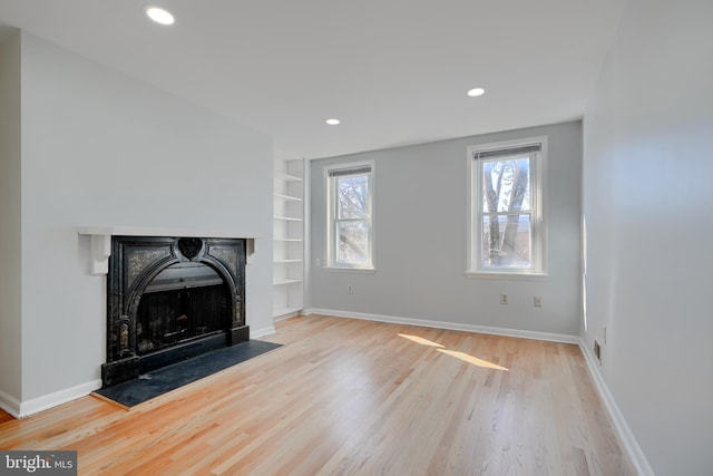 living room featuring light wood finished floors, built in shelves, baseboards, and a fireplace