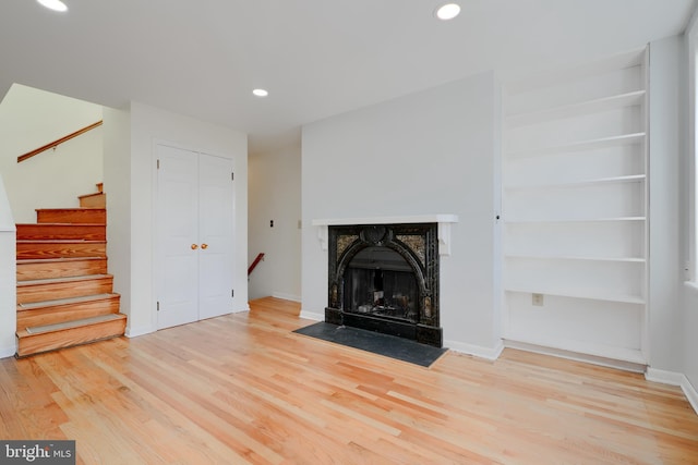 unfurnished living room featuring light wood finished floors, baseboards, a fireplace with flush hearth, stairs, and recessed lighting