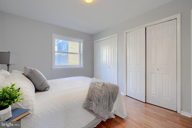 bedroom with light wood-type flooring, baseboards, and multiple closets