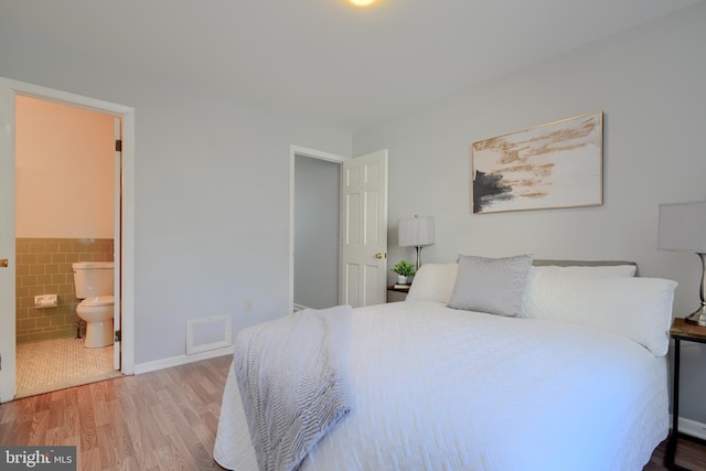 bedroom featuring ensuite bath, light wood-style flooring, tile walls, and wainscoting