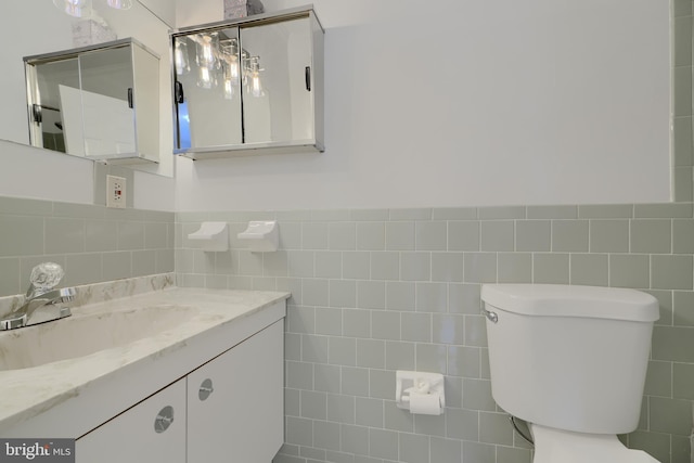 half bathroom with toilet, wainscoting, tile walls, and vanity