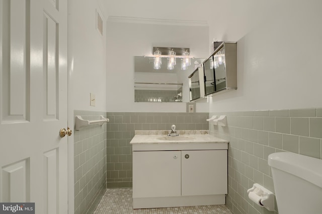 bathroom with toilet, vanity, tile walls, wainscoting, and crown molding