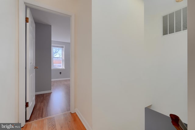 hall with light wood finished floors, baseboards, visible vents, and a heating unit