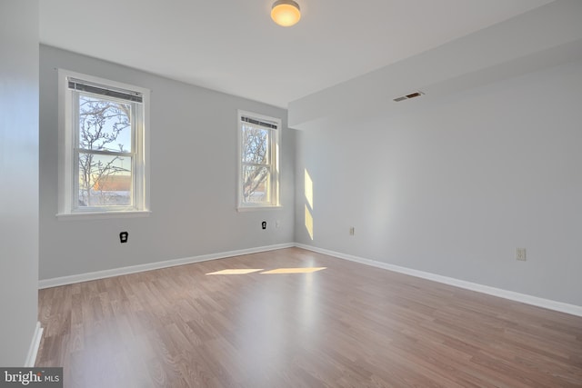 empty room with light wood-type flooring, visible vents, and baseboards