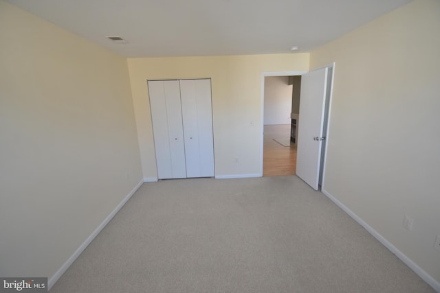 unfurnished bedroom featuring a closet, light colored carpet, visible vents, and baseboards