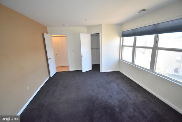 unfurnished bedroom with baseboards, visible vents, dark colored carpet, and a closet