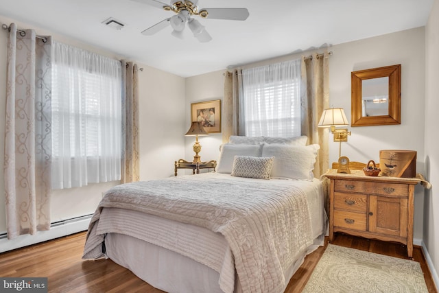 bedroom with a baseboard heating unit, wood finished floors, visible vents, and a ceiling fan