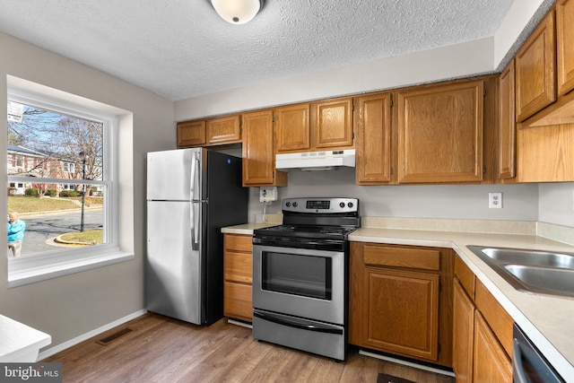 kitchen featuring brown cabinetry, visible vents, stainless steel appliances, light countertops, and under cabinet range hood