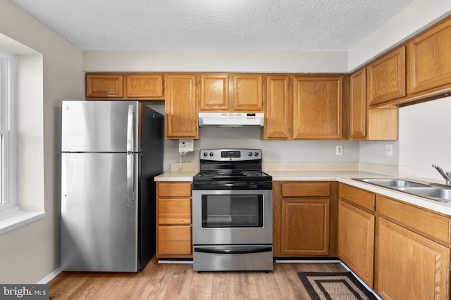 kitchen with a sink, light countertops, under cabinet range hood, and stainless steel appliances