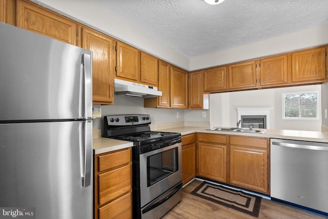 kitchen with under cabinet range hood, appliances with stainless steel finishes, light countertops, and wood finished floors