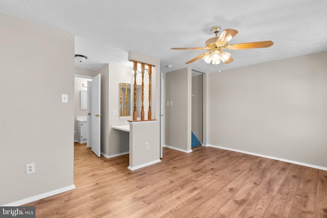 unfurnished living room featuring a ceiling fan, wood finished floors, baseboards, and a textured ceiling