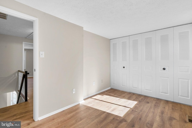 unfurnished bedroom with visible vents, baseboards, a textured ceiling, and wood finished floors