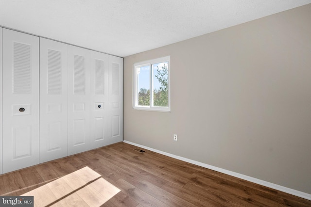 unfurnished bedroom featuring visible vents, a textured ceiling, wood finished floors, a closet, and baseboards