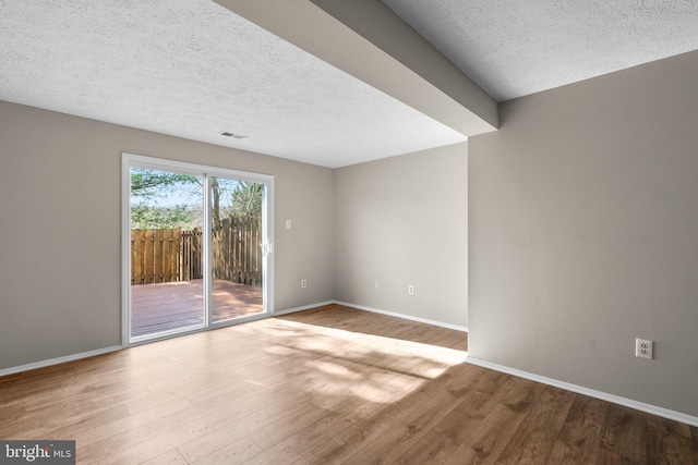 empty room featuring visible vents, wood finished floors, baseboards, and a textured ceiling