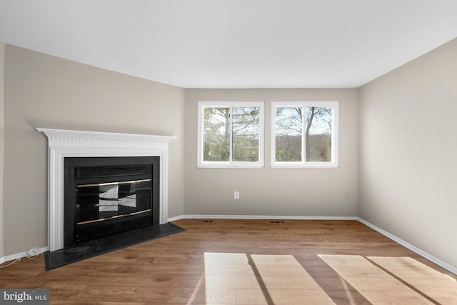 unfurnished living room featuring a glass covered fireplace, baseboards, and wood finished floors