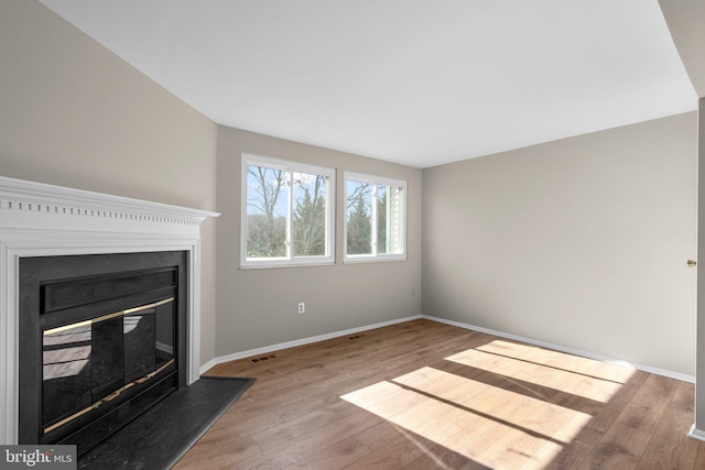 unfurnished living room featuring a glass covered fireplace, baseboards, visible vents, and wood finished floors