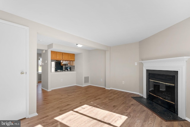 unfurnished living room featuring a glass covered fireplace, light wood-style floors, visible vents, and baseboards