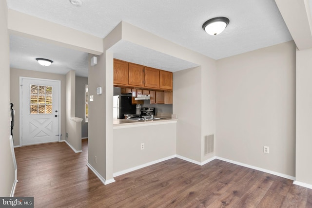 kitchen with visible vents, under cabinet range hood, stainless steel electric stove, freestanding refrigerator, and brown cabinetry