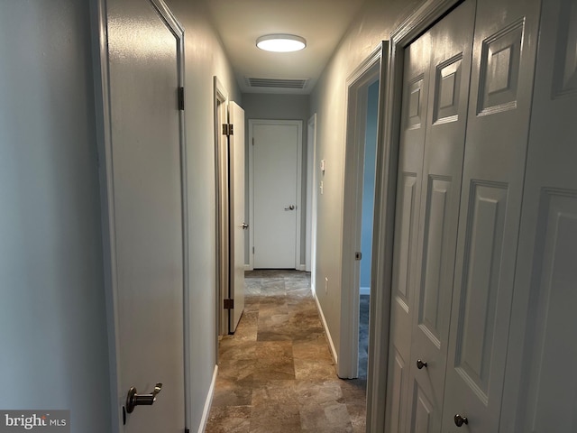 hall featuring stone finish floor, baseboards, and visible vents