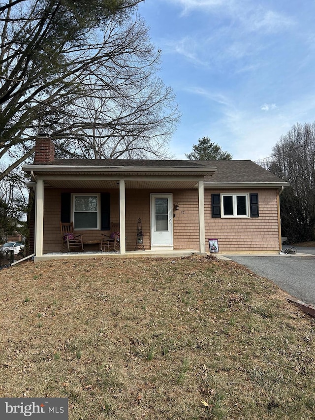 single story home featuring driveway, a porch, a chimney, and a front yard