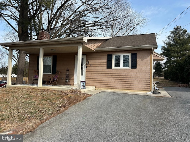 single story home with a porch, a chimney, driveway, and a shingled roof