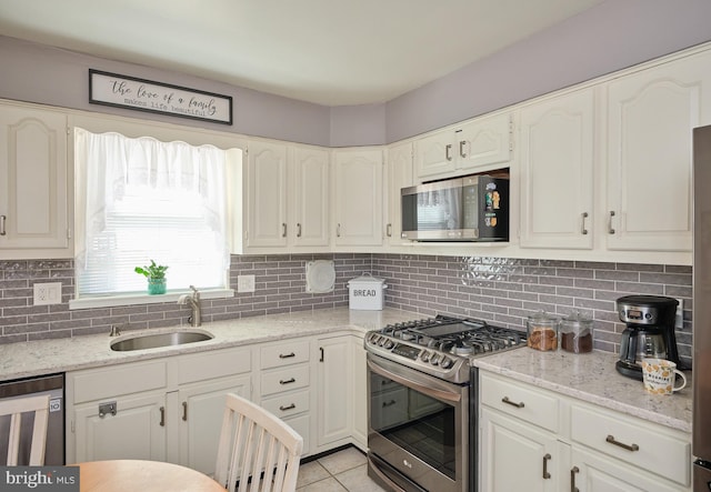 kitchen with appliances with stainless steel finishes, a sink, white cabinetry, and light stone countertops