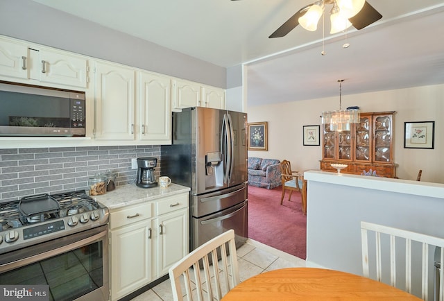 kitchen with light tile patterned floors, tasteful backsplash, light colored carpet, appliances with stainless steel finishes, and decorative light fixtures