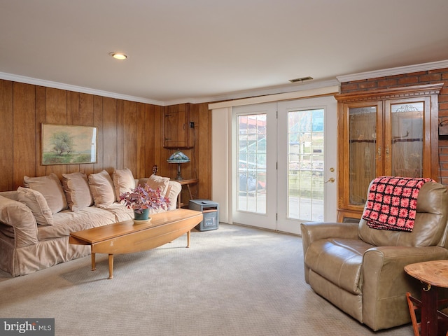 living area with ornamental molding, wood walls, visible vents, and light colored carpet